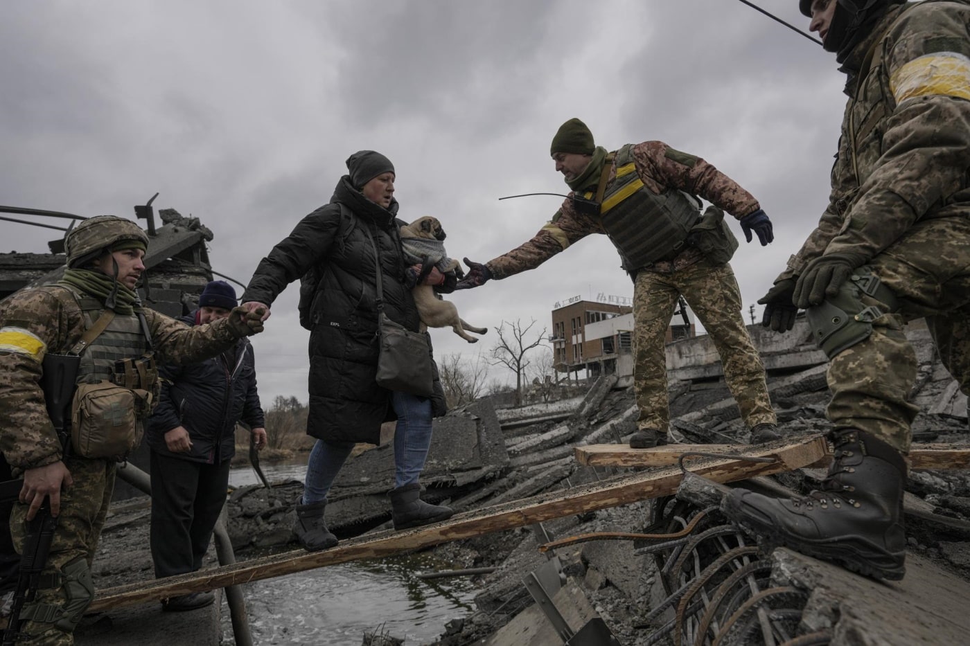 Ukrainian servicemen help a woman carrying a small dog across the Irpin River on an improvised path while assisting people fleeing the town of Irpin, Ukraine, Saturday, March 5, 2022. (AP Photo - Vadim Ghir
