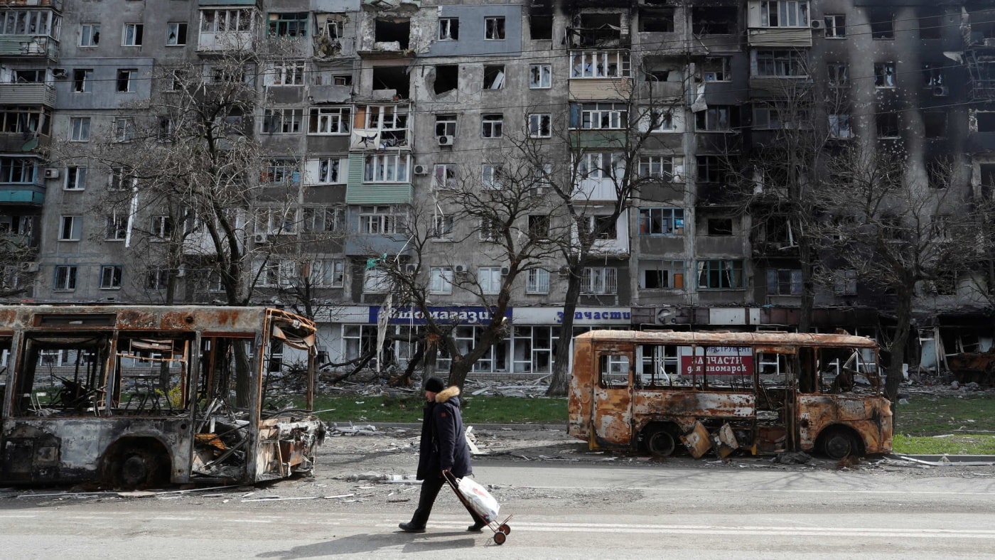 A resident walks along a street past burnt out buses in Mariupol on April 19. - Reuters