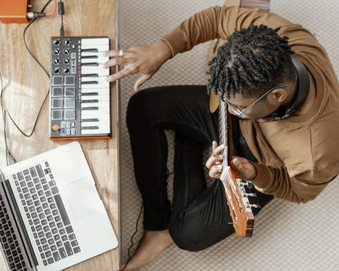 Top view of male musician at home playing guitar and mixing with laptop